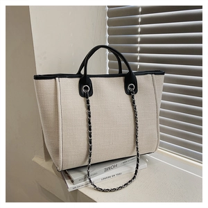 Close-up of beige woven bucket bag with black leather trim and metal chain strap