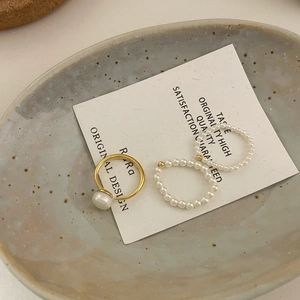 Close-up of elegant mini pearl ring set with gold band and beaded elastic strands