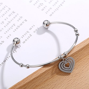 Detail of silver stainless steel open bangle with a triple-layered heart charm pendant