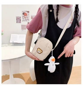 Detail of cream corduroy crossbody bag with bear embroidery and plush duck charm