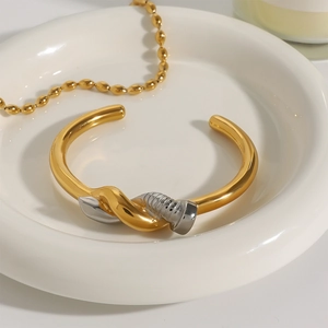 Macro shot of two-tone gold and silver nail bracelet on a white ceramic plate