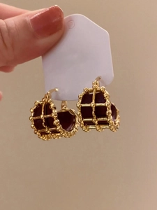 Detail of gold plated round cage hoop earrings with red leather inlay on a white card