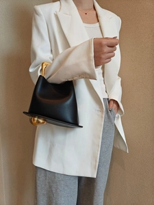 Model holding a vintage black leather bucket bag with architectural gold metal handles