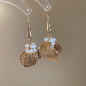 Detail of gold hollow petal earrings with hanging pearls on a warm beige background