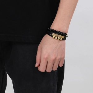 Detail of men's multilayered black leather bracelet with gold metal tubes on wrist
