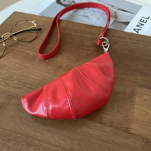 Vue de dessus du sac croissant rouge plissé avec boucles argentées sur fond en bois