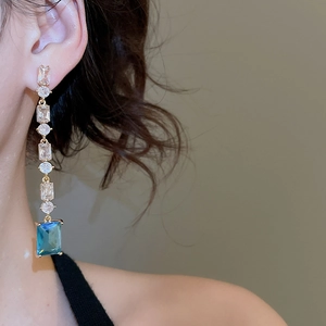 Detail of long drop earrings with gold plating and emerald green rectangle zircon