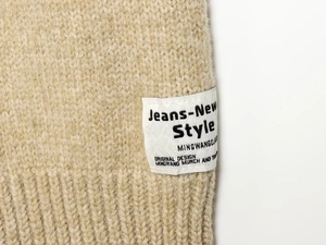Close-up of beige knit jacket detail featuring ribbed texture and stylish woven brand tag