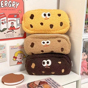Three plush cookie pencil cases with cute expressions stacked against a warm background