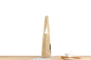 Vue latérale du sac cabas en paille tressée beige sur table avec accessoires café