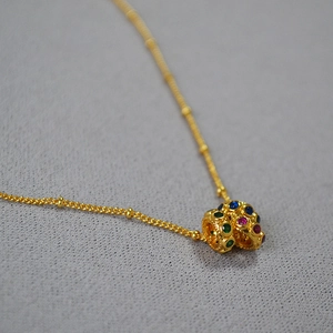 Vue macro d'un pendentif barillet doré serti de zircons colorés sur une chaîne perlée