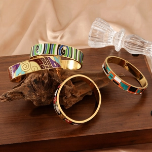 Artistic enamel bracelets with Klimt-style patterns displayed on wood and crystals