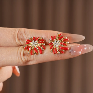 Close-up of golden fireworks earrings with red enamel petals and clear crystal center