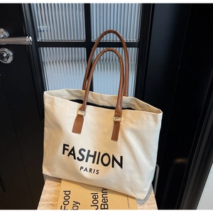 Detail einer großen Canvas-Einkaufstasche mit braunen Ledergriffen und Fashion Paris Aufdruck