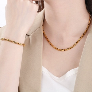 Elegant gold chain necklace and bracelet set shown on model in a minimalist beige outfit
