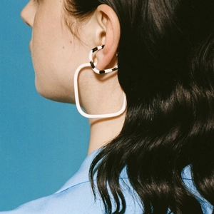 Detail of square zebra pattern clip earrings in stainless steel on a blue background