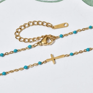 Macro shot of gold cross pendant necklace with blue beads and adjustable lobster clasp