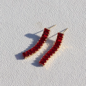 Golden earrings set with curved rectangular red zircon crystals on a white surface