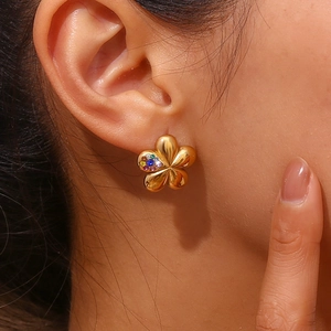 Detail of 18K gold flower stud earrings with colorful gemstones worn on the ear
