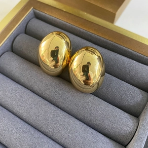 Macro shot of polished gold oval stud earrings resting on a grey velvet jewelry box