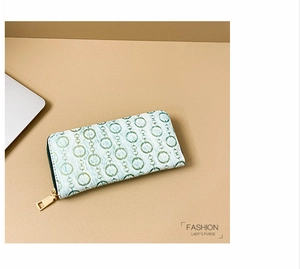 Detail of long women's wallet with green ring pattern and golden zipper on brown surface