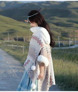Detail van gebreide poncho met witte faux fur rand en pom-pom kwastjes op de prairie