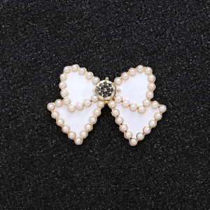 Macro detail of white enamel bow charm with pearl border and center rhinestone