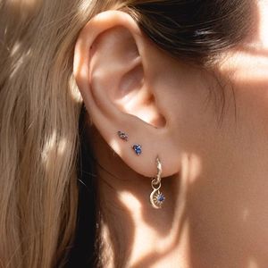 Close-up of elegant gold earrings with blue stones and moon sun charms on model ear