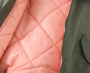 Detail of olive green jacket with pink diamond quilted lining and metal zipper