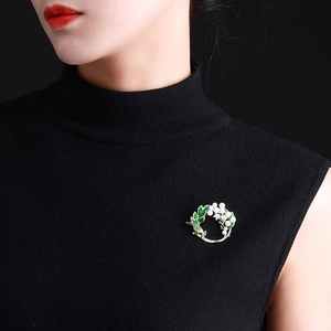 Exquisite pearl and green leaf brooch worn on a black knit top, detailed jewelry closeup