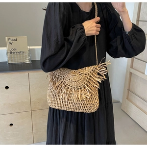 Detail of a straw crossbody bag featuring boho fringe trim and a thin woven shoulder strap
