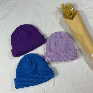 Close-up of knitted beanies in dark purple, light purple and blue on white fabric