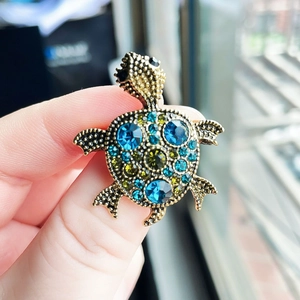 Vintage golden turtle brooch with blue and green crystals held by hand in natural light