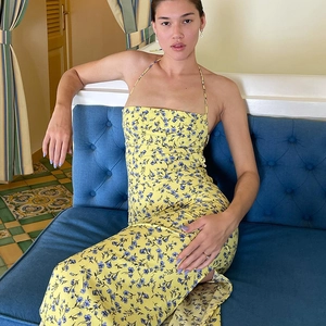 Floral backless slit sundress in yellow and blue, worn by a model on a blue sofa