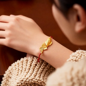 Close-up of a vintage koi fish gold pendant with a delicate red braided rope bracelet