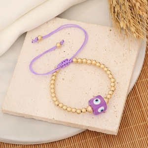 Purple woven evil eye bracelet with gold beads displayed on an aesthetic stone surface