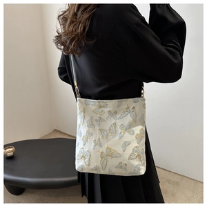 Detail of white satin shoulder bag with gold and blue butterfly embroidery on model