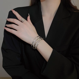 Detail of silver bamboo texture stacked bracelets and ring on black suit sleeve