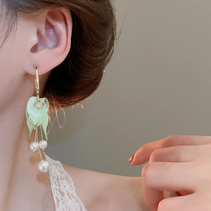 Close-up of green flower earrings with white pearl tassels and golden metal chain