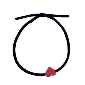 Detail of black elastic hair tie with a small red heart pendant charm on white background