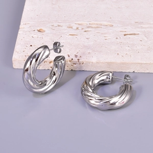 Detailed view of silver stainless steel twisted hoop earrings on a beige stone slab
