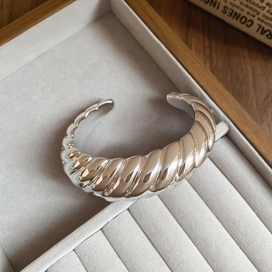 Macro detail of silver croissant twist bangle with a polished mirror finish on jewelry tray