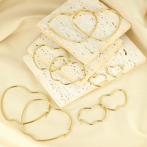 Detailed view of five sizes of polished gold heart-shaped hoop earrings on elegant silk