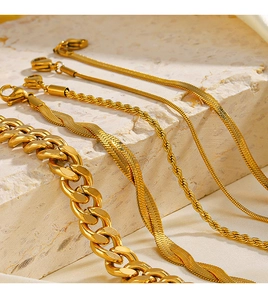 Detailed macro view of 18K gold plated Cuban and snake chains on textured stone base