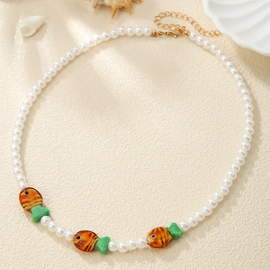 Detail of colorful beaded fish necklace with pearls and sea charms on a beige surface