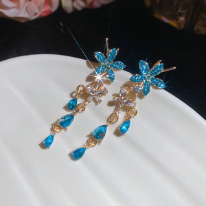 Close-up of blue crystal flower earrings with waterdrop tassels on a white shell tray