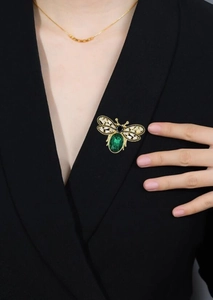 Close-up of golden bee brooch with green crystal on a black suit lapel detail