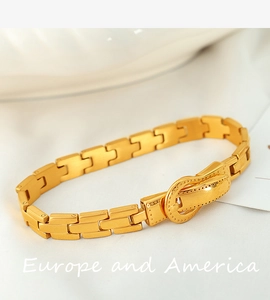 Macro detail of gold watchband style bracelet with a belt buckle clasp on white silk
