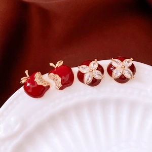 Detail of 18k gold plated apple and flower stud earrings on a white ceramic plate