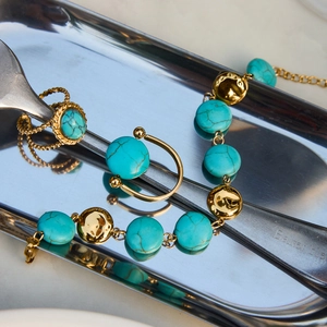 Detailed close-up of gold titanium steel jewelry set with turquoise on minimalist tableware